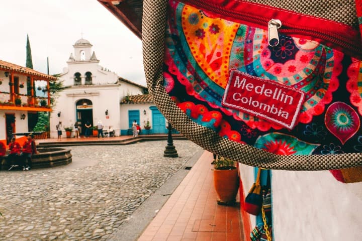 riñonera en primer plano con escrito medellin colombia y iglesia de fondo en pueblito paisa