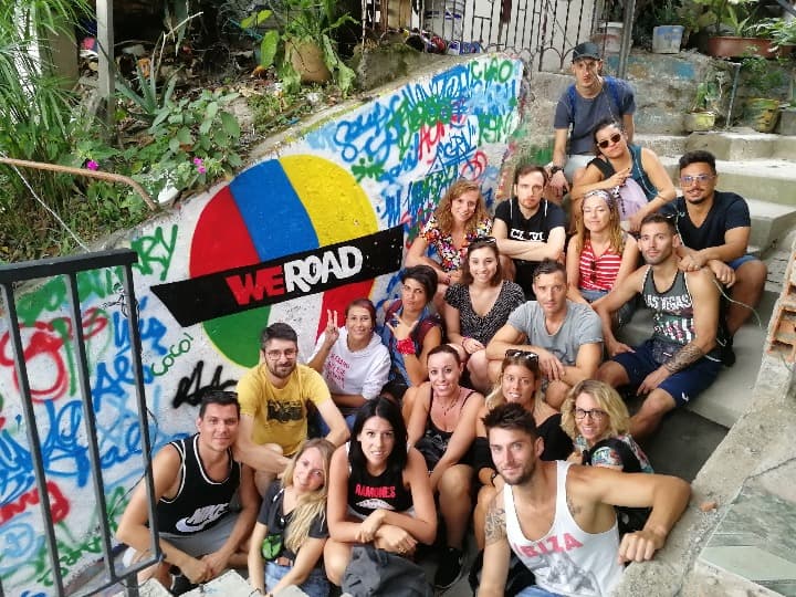 foto de grupo de chicos de weroad sentados delante de un graffiti en la comuna 13, algo que ver en medellín