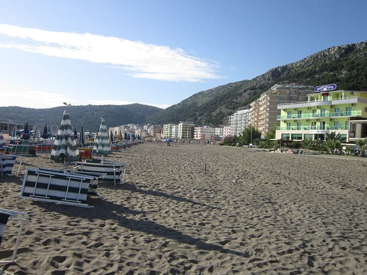 sombrillas y tumbonas y edificios al fondo en la playa de shengjin