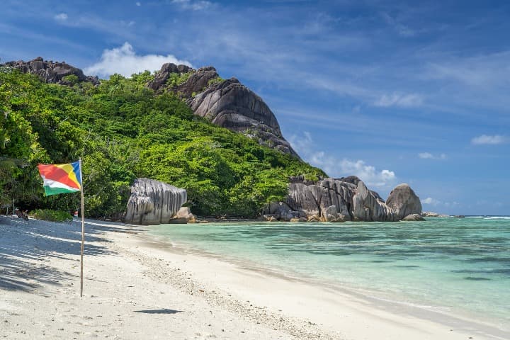 playa de seychelles con bandera, montaña con árboles al fondo