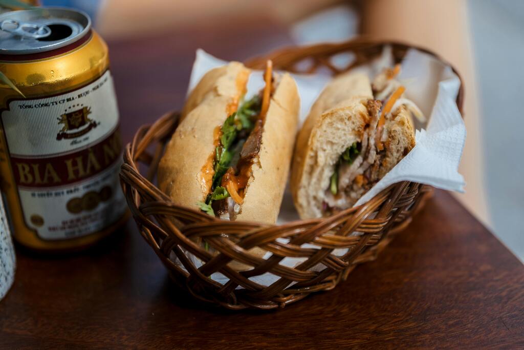 Un cesto con banh mi, el emblemático sándwich vietnamita, servido con una lata de cerveza local, perfecto para una comida callejera.