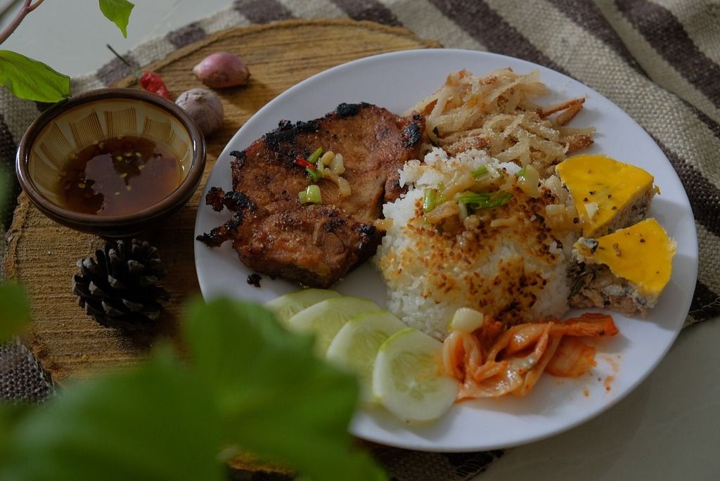 Cơm Tấm, un plato típico vietnamita que incluye arroz, carne de cerdo a la parrilla y otros acompañamientos, representando la diversidad de sabores locales.