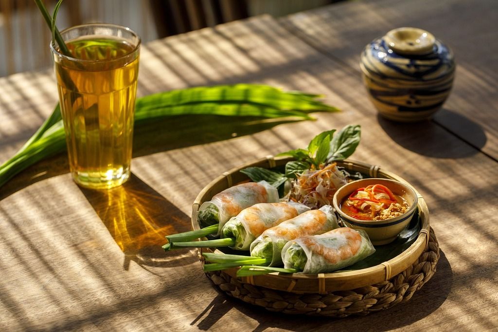 Un plato de rollitos vietnamitas frescos rellenos de camarón, acompañado de salsa de maní, servido con té helado.