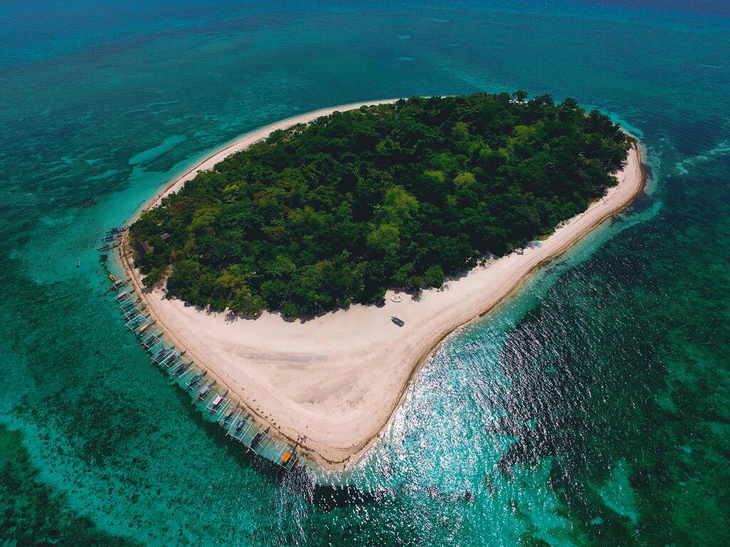 Vista aérea de una isla tropical en Filipinas rodeada de aguas cristalinas y playas de arena blanca.