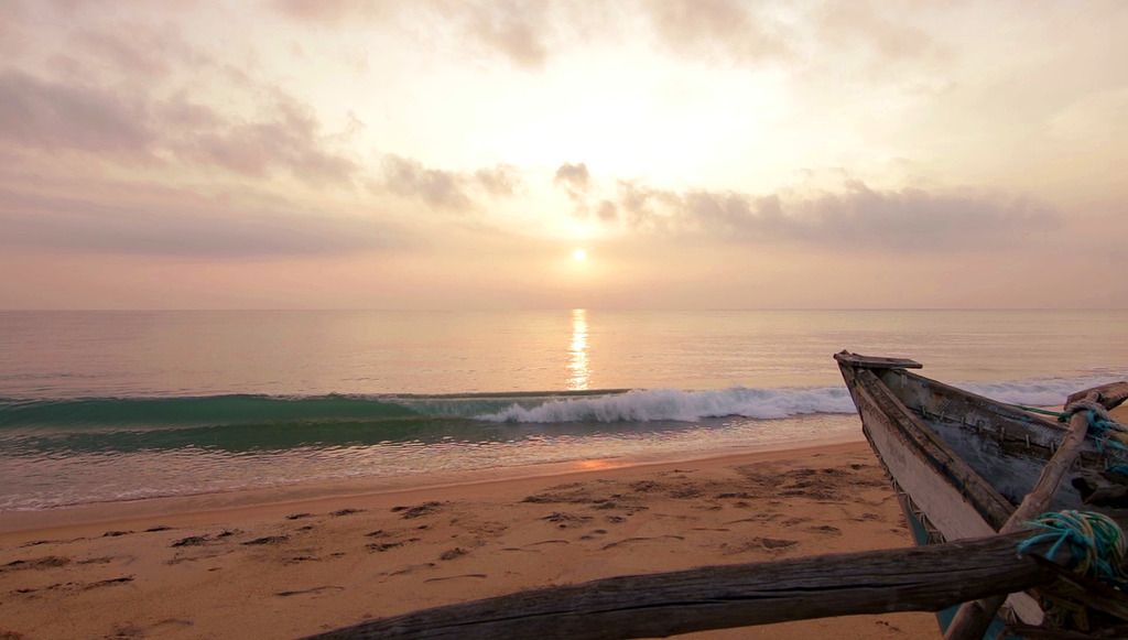 Puesta de sol en una playa tranquila con una barca de madera en primer plano.