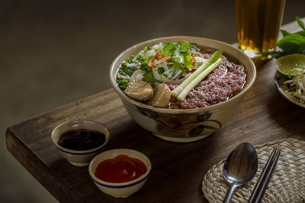 Un delicioso plato de pho, la tradicional sopa vietnamita con fideos de arroz, carne y hierbas frescas, acompañado de salsas típicas.