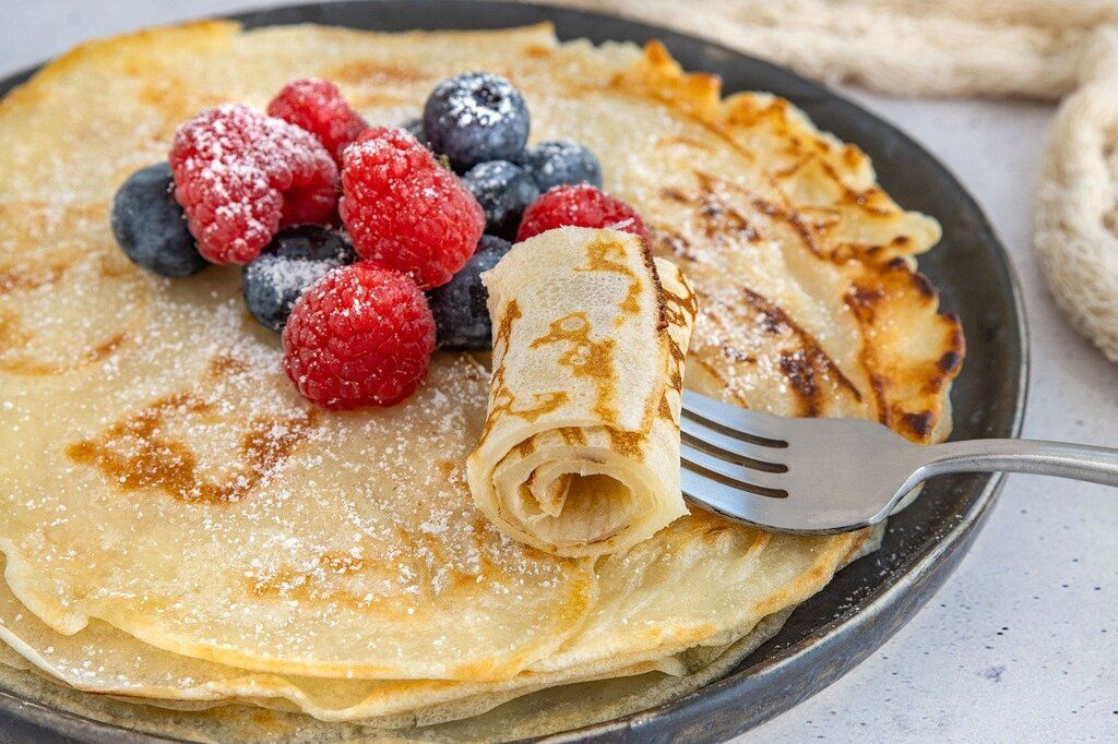 Crepas dulces servidas con frambuesas, arándanos y azúcar glas.