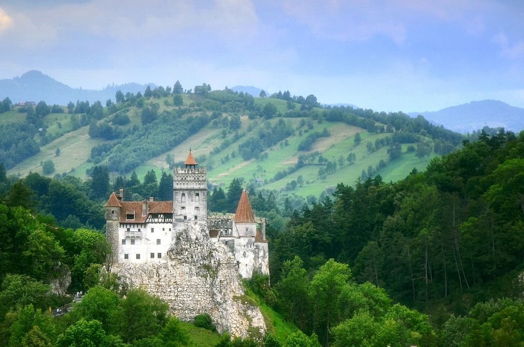 El Castillo de Bran en Rumanía rodeado de montañas verdes y un cielo despejado.