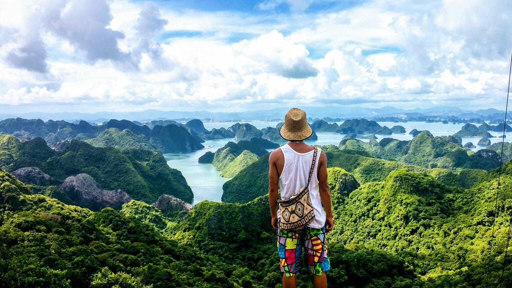 Explorador con sombrero mirando el paisaje de la bahía de Halong en Vietnam, rodeada de montañas verdes.
