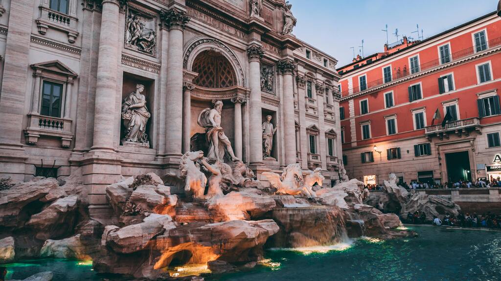 La Fontana di Trevi iluminada al anochecer con detalles arquitectónicos.
