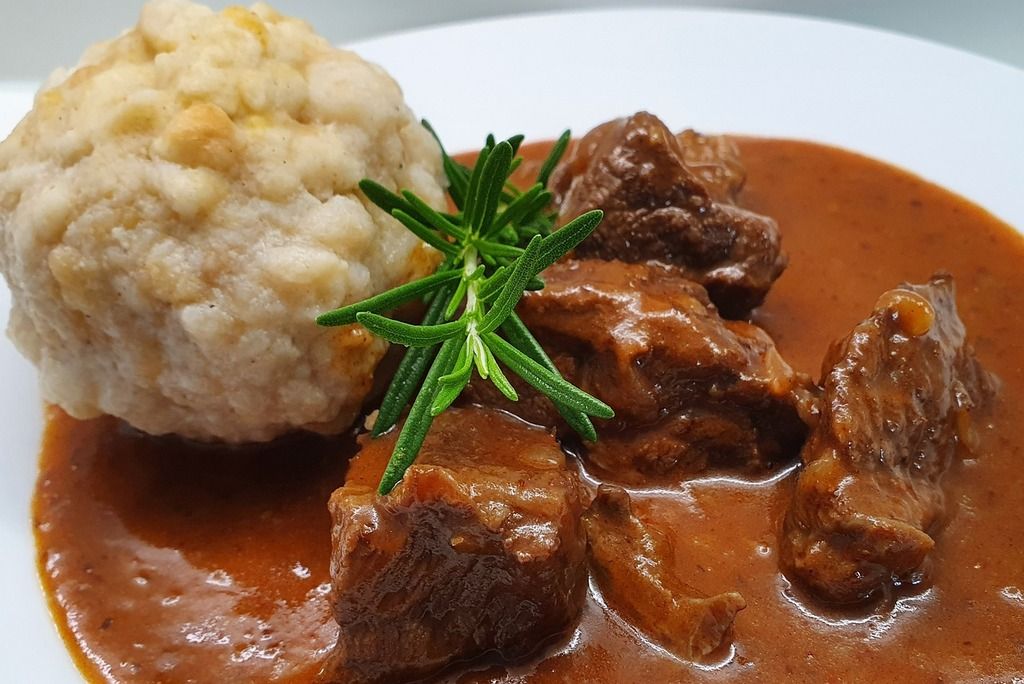 Plato típico húngaro con guiso y albóndiga de pan servido en un plato blanco.