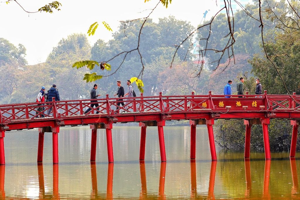 Puente Rojo Huc en el lago Hoan Kiem, Hanoi, rodeado de árboles y reflejado en el agua tranquila.