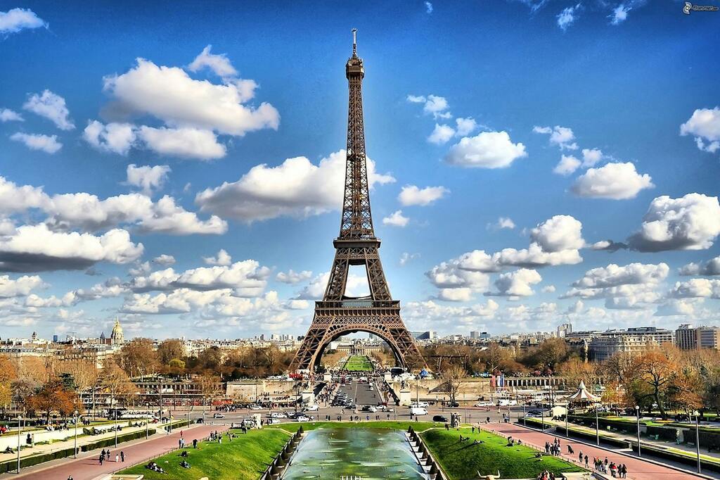 La Torre Eiffel en París en un día soleado con cielo despejado y nubes esponjosas.