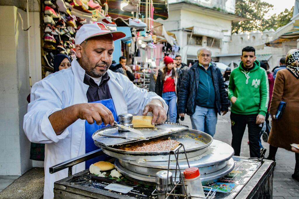 Un vendedor callejero preparando comida tradicional en un mercado bullicioso de Marruecos.