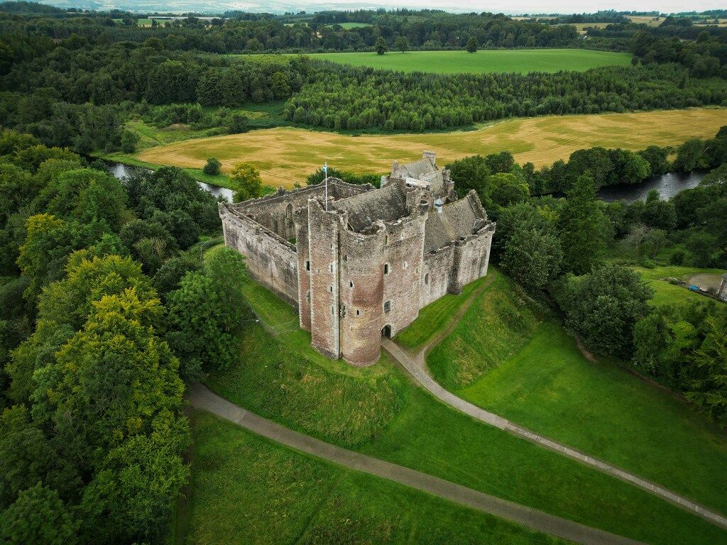 Vista aérea de un castillo medieval escocés rodeado de campos y bosques verdes