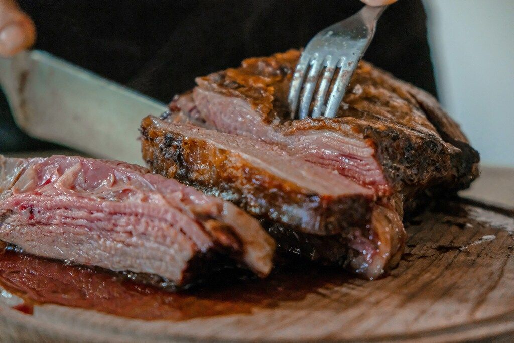 Carne asada jugosa siendo cortada sobre una tabla de madera