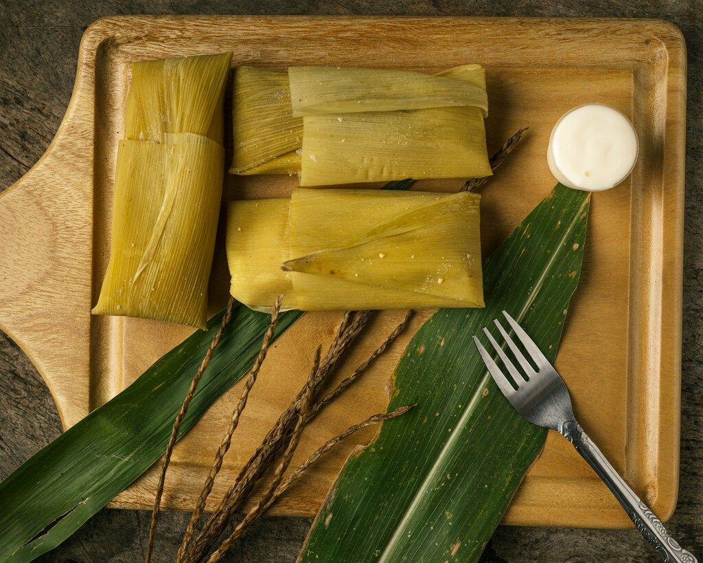 Tamales envueltos en hojas de maíz servidos con crema