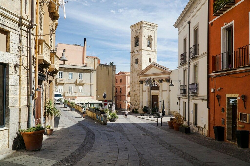 Calle del casco antiguo de Cagliari con una iglesia y edificios históricos pintados en tonos cálidos