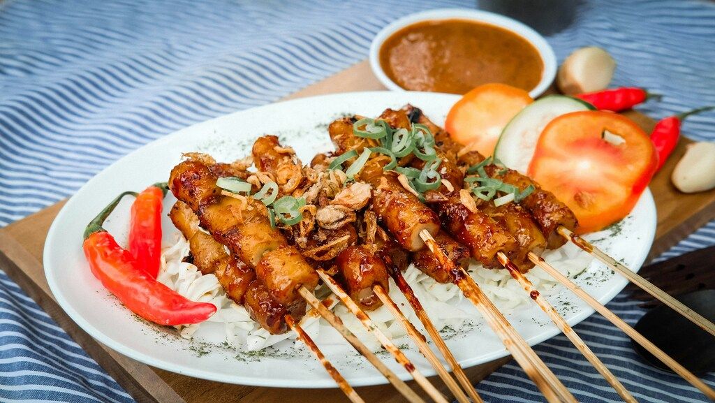 Plato de brochetas de pollo satay con cebolla frita, chiles rojos y salsa de cacahuete.