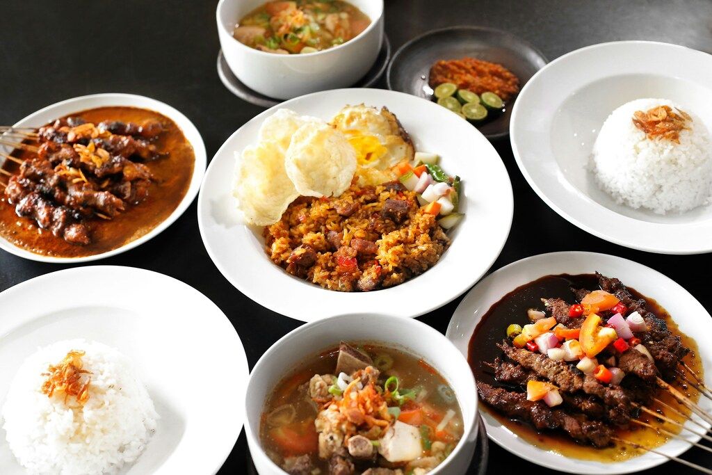 Mesa llena de platos típicos indonesios con arroz, sopas y satay en salsa.