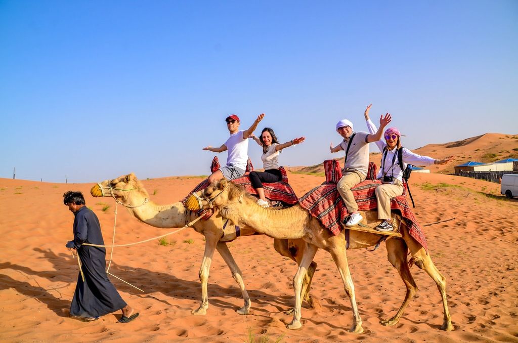 Grupo de viajeros WeRoad montando camellos guiados por un beduino en el desierto.
