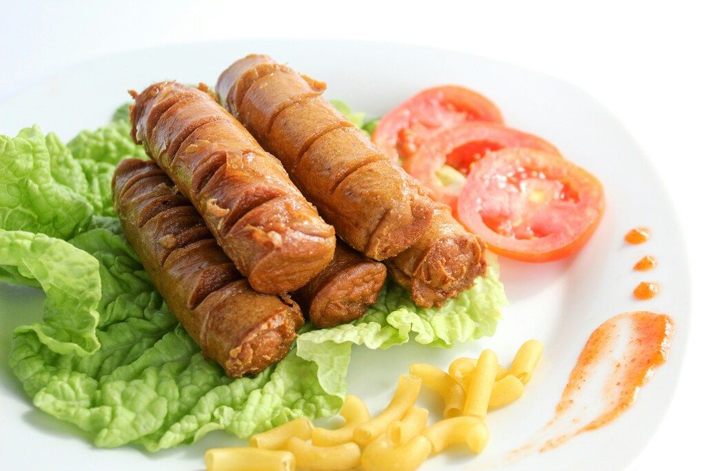 kranjska klobasa servidas con lechuga, tomate y pasta corta en un plato blanco
