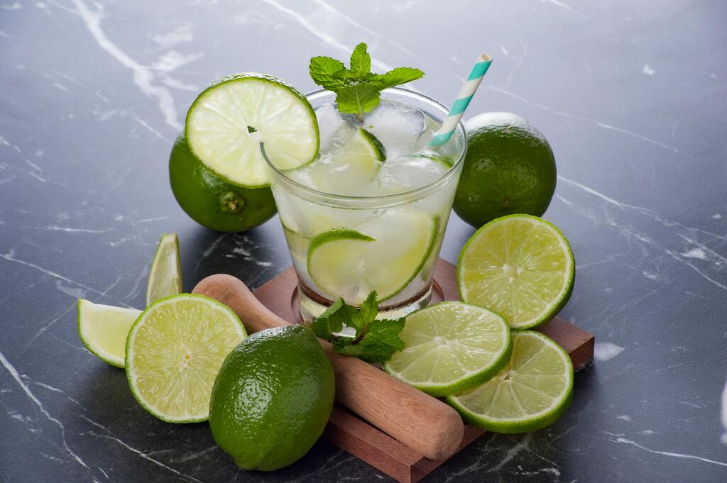 Caipirinha brasileña servida con rodajas de lima fresca y una pajilla a rayas sobre fondo de mármol