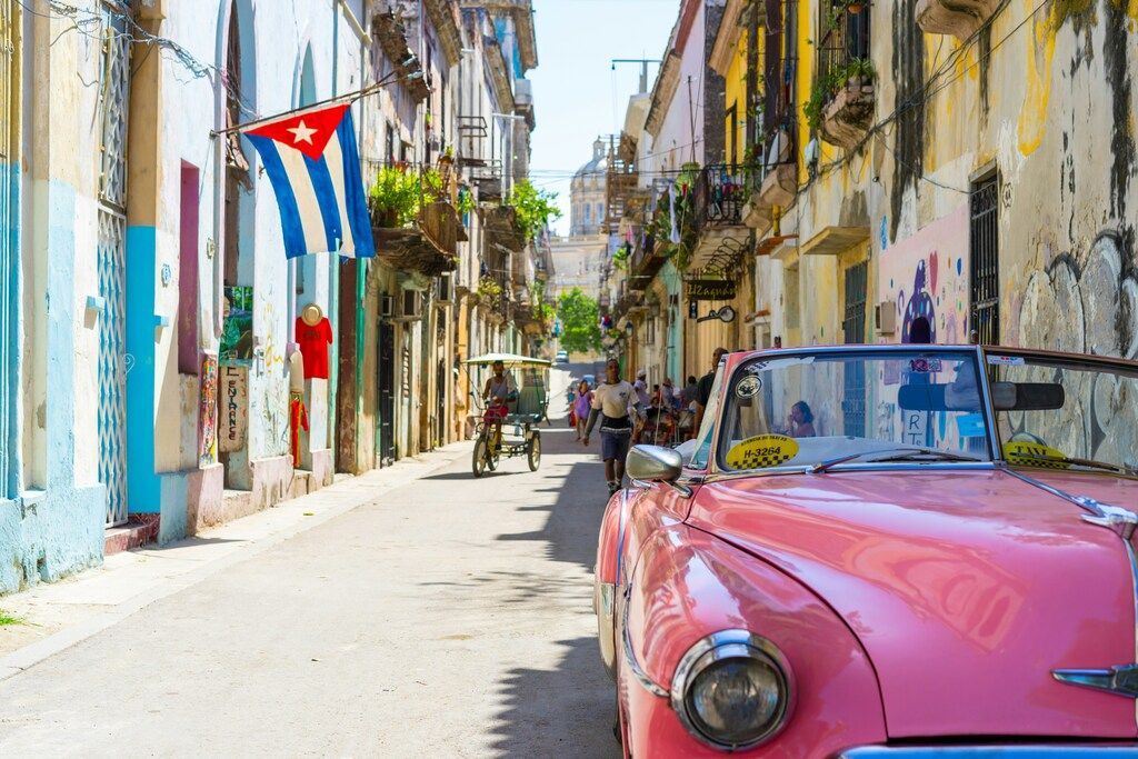 Calle colorida en La Habana con coche clásico rosa y bandera cubana