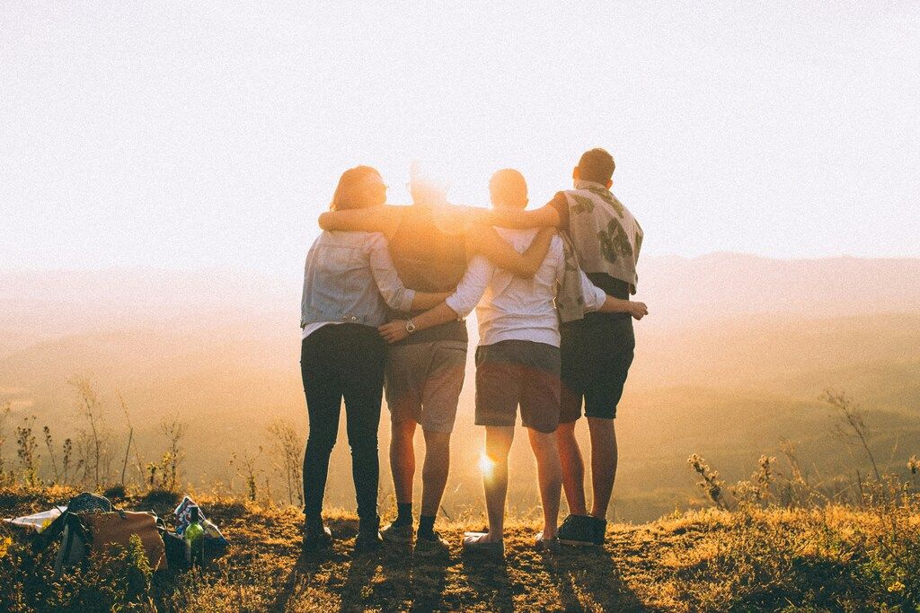 Cuatro viajeros abrazados mientras contemplan el atardecer desde lo alto de una colina, en un momento de conexión y amistad.