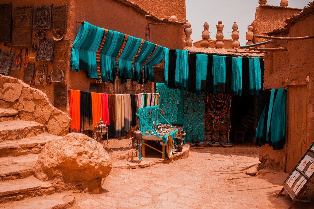 Puesto artesanal en un zoco marroquí con telas color turquesa, joyas y objetos tradicionales colgados en las paredes.