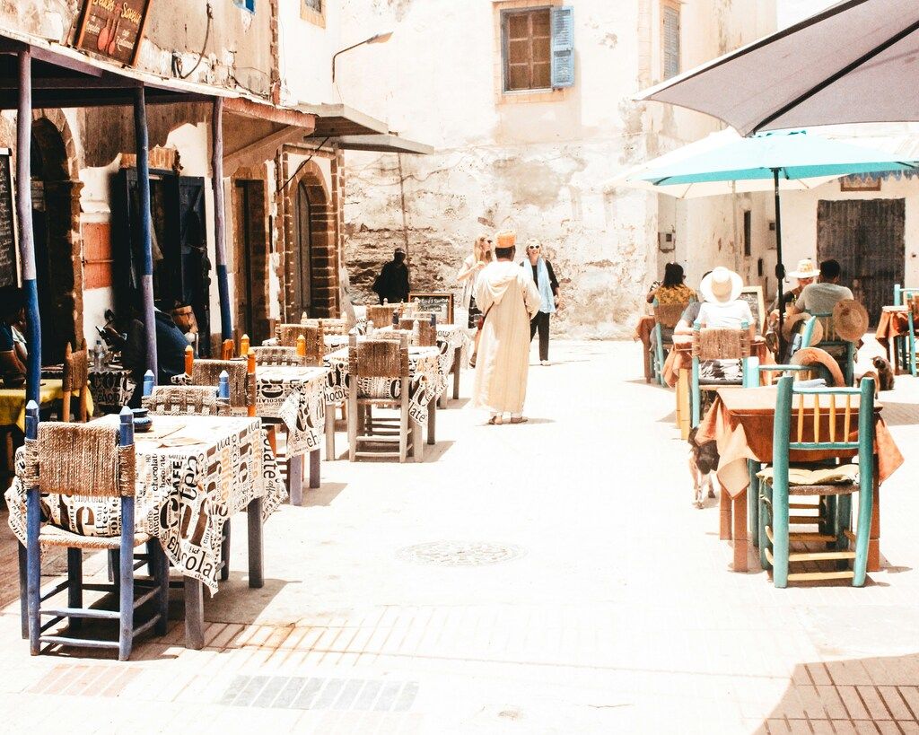 Restaurante al aire libre con mesas dispuestas en una plaza soleada, rodeada de edificios de estilo marroquí.