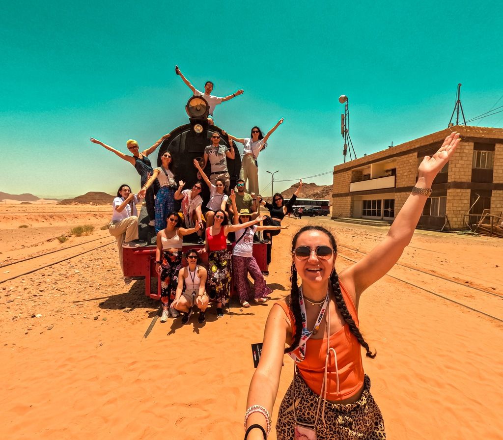 Grupo de viajeros WeRoad posando con entusiasmo sobre una locomotora antigua en medio del desierto, bajo un cielo turquesa brillante.
