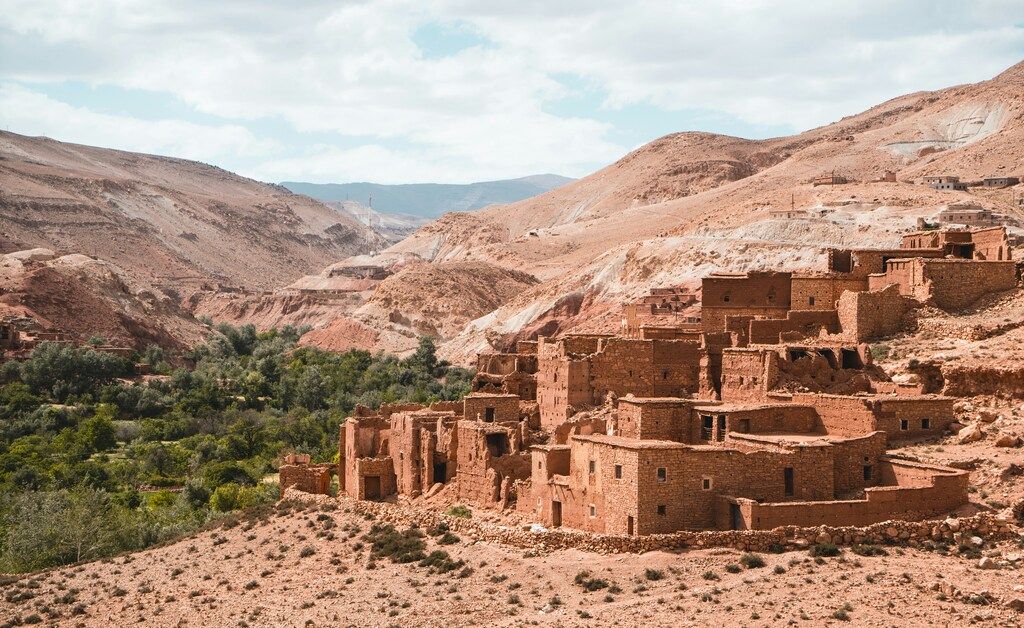Antiguo pueblo de adobe enclavado en las montañas del Atlas rodeado de paisajes áridos y verdes.