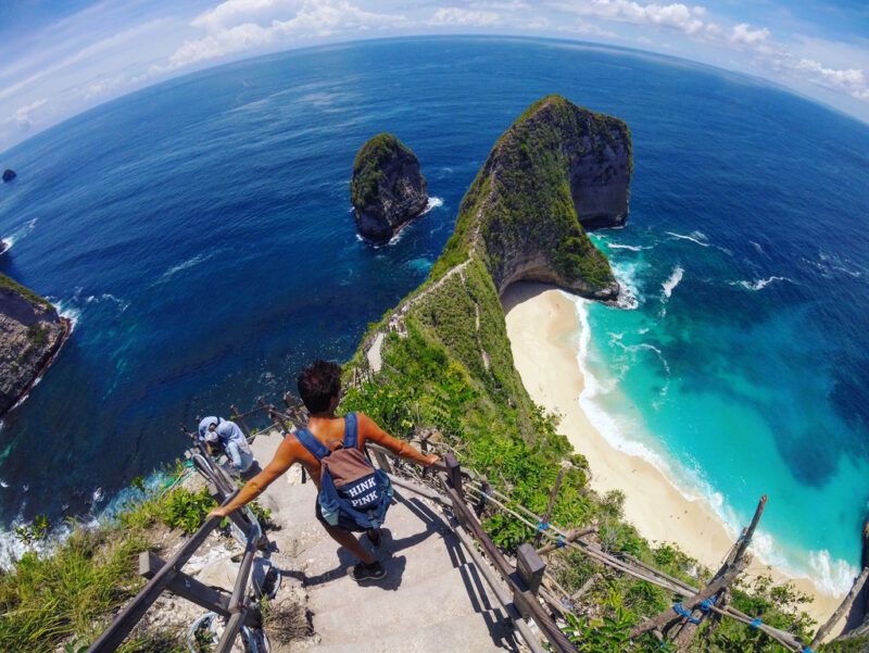 Caminante en un acantilado en la isla de Nusa Penida, Indonesia, con vistas a la famosa playa de Kelingking y a la formación rocosa con forma de T-Rex. Caminante en un acantilado en la isla de Nusa Penida, Indonesia, con vistas a la famosa playa de Kelingking y a la formación rocosa con forma de T-Rex.