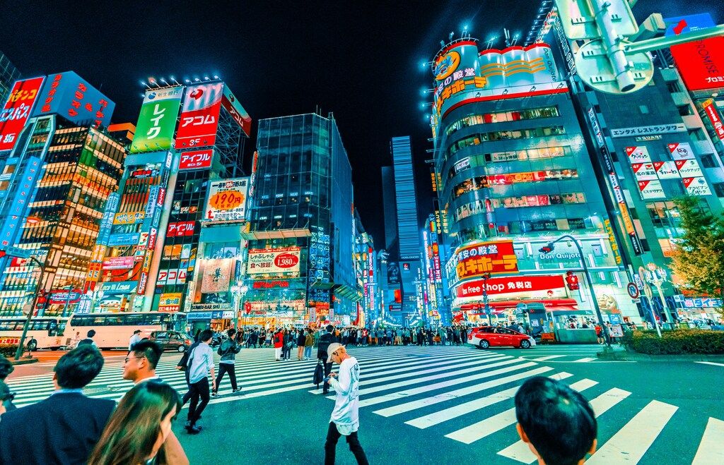 Calles iluminadas de Shinjuku con carteles de neón y mucha gente cruzando el paso de peatones.