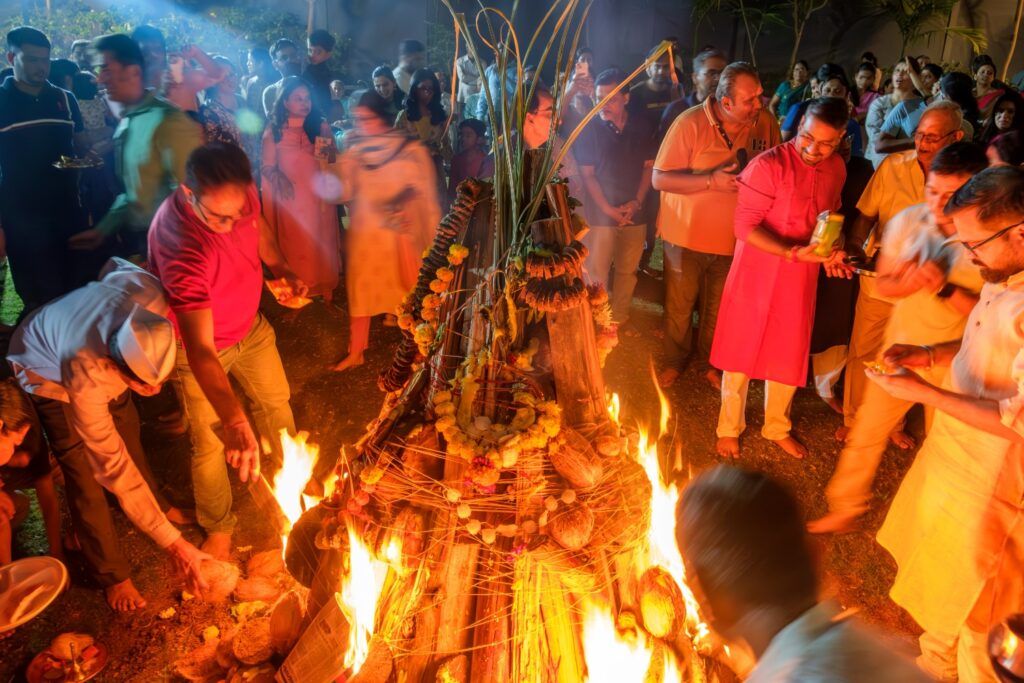 Personas reunidas alrededor de una hoguera decorada con flores durante la noche de Holika Dahan, el ritual que marca el inicio del festival Holi en India.