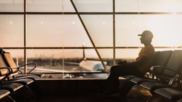chico con gorro sentado en un aeropuerto, ventanal al fondo con avion en pista