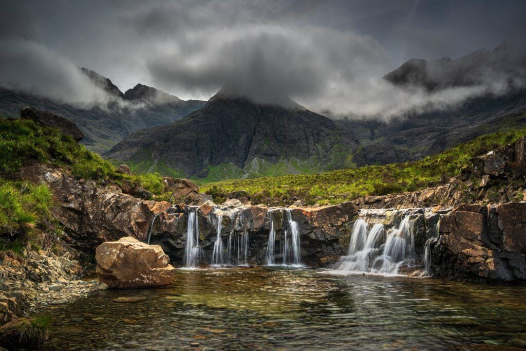 Cascada en las Fairy Pools con aguas cristalinas, rocas y montañas Cuillin cubiertas por niebla en la Isla de Skye.