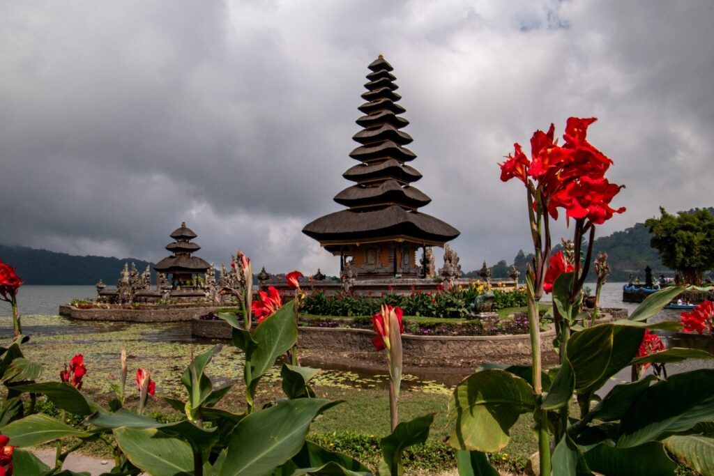Templo Pura Ulun Danu Beratan en el lago Bratan visto a través de flores rojas.