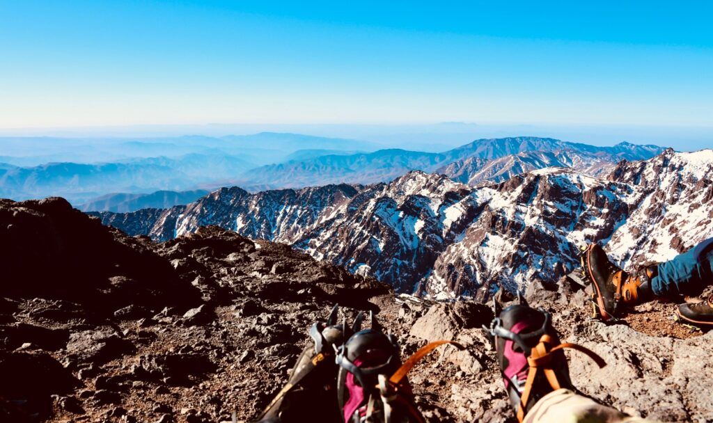 Vista desde la cumbre nevada del Atlas, mostrando botas de montaña y crampones en primer plano.