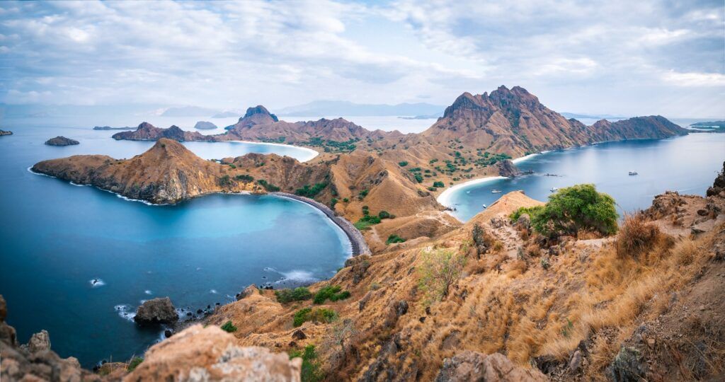 Impresionante vista panorámica del paisaje montañoso y árido de las islas de Komodo (cerca de Bali), que muestran bahías de arena blanca y agua turquesa brillante en un día nublado.