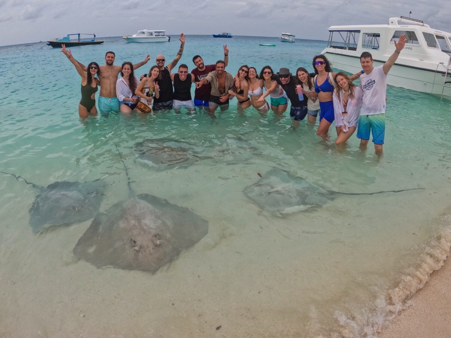 Un groupe de voyageurs WeRoad pose en souriant dans les eaux cristallines des Maldives, entourés de raies manta.