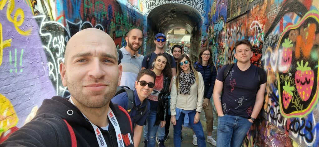 Grupo de viajeros de Weroad posando y sonriendo en un túnel estrecho cubierto de vibrantes grafitis en Bruselas.