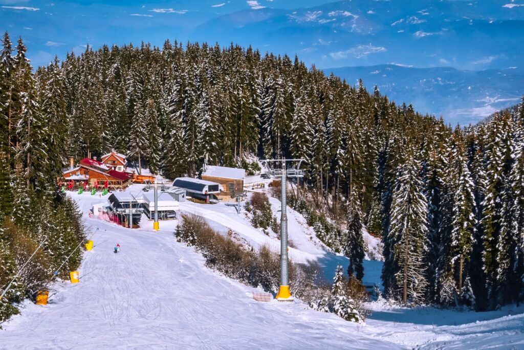Pista de esquí en Bansko, Bulgaria, con telesilla y edificios de madera en un bosque nevado.