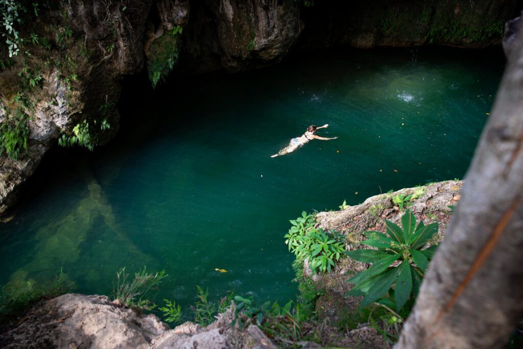 Vista aérea de una mujer nadando en una piscina natural de agua verde esmeralda en un cenote o cascada cubana.