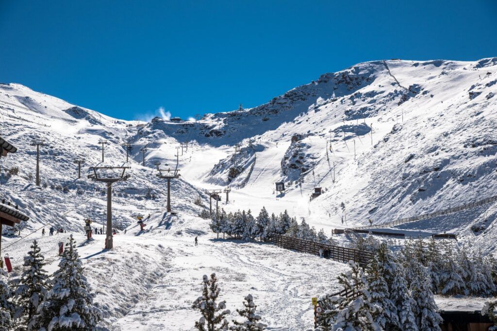 Montaña de Sierra Nevada cubierta de nieve con varias pistas y remontes activos bajo el intenso sol de Andalucía.