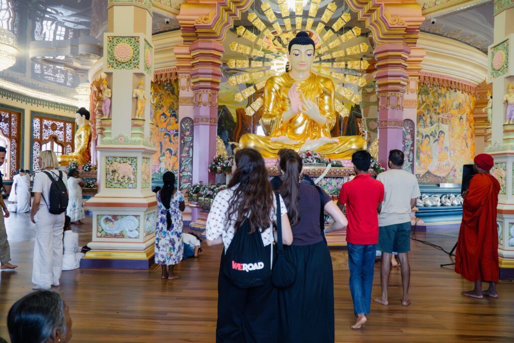 Un grupo de mujeres visitan un templo budista en Sri Lanka, contemplando una gran estatua dorada de Buda rodeada de decoraciones coloridas.