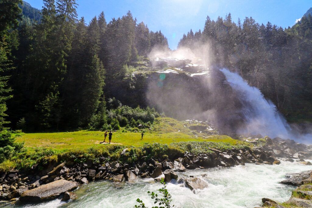 La majestuosa cascada de Krimml cayendo con fuerza entre un bosque de pinos, con un río caudaloso en primer plano en Austria.