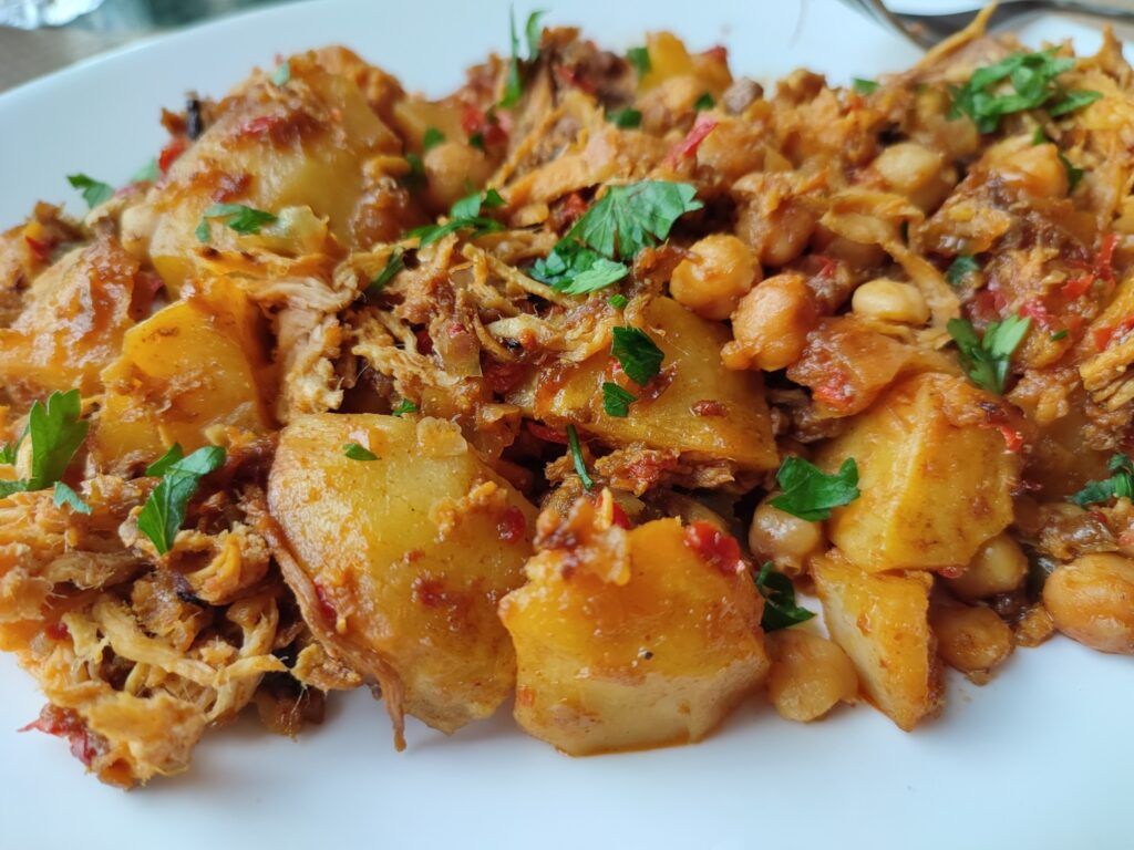 Un primer plano de Ropa Vieja, un plato tradicional cubano con carne desmenuzada, patatas, garbanzos y perejil fresco.