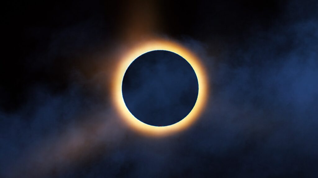 Un eclipse solar total con una corona brillante de fuego alrededor de la luna negra en un cielo oscuro.